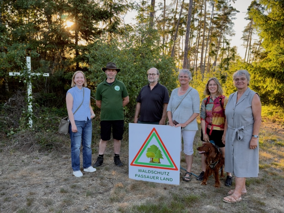 Feiern 1 Jahr Prozession in Marterberg: Grüne & Bürgerinitiative Sechs Personen stehen in einer Lichtung im Wald. Vor ihnen steht eine Tafel mit der Aufschrift "Waldschutz Passauer Land".