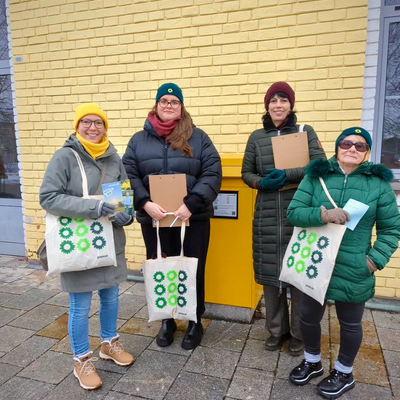 Vier Personen posieren für ein Foto. Sie tragen Winterbekleidung. Sie halten Taschen mit der Aufschrift „gruene.de“