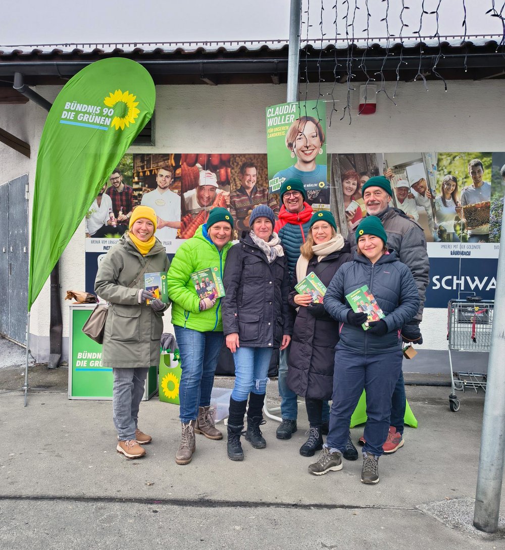 Sieben Personen posieren vor einem Infostand der Partei Bündis 90/Die Grünen. Sie tragen Winterbekleidung.