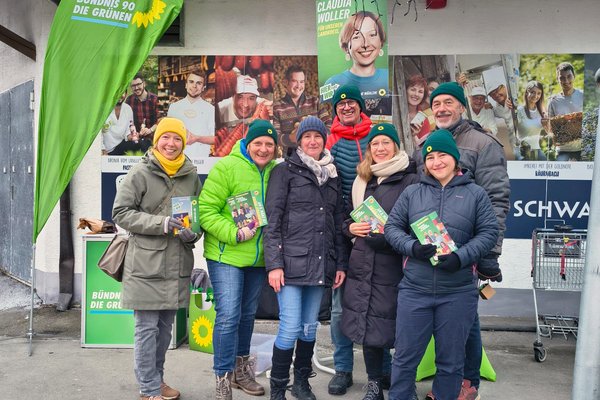 Sieben Personen posieren vor einem Infostand der Partei Bündis 90/Die Grünen. Sie tragen Winterbekleidung.