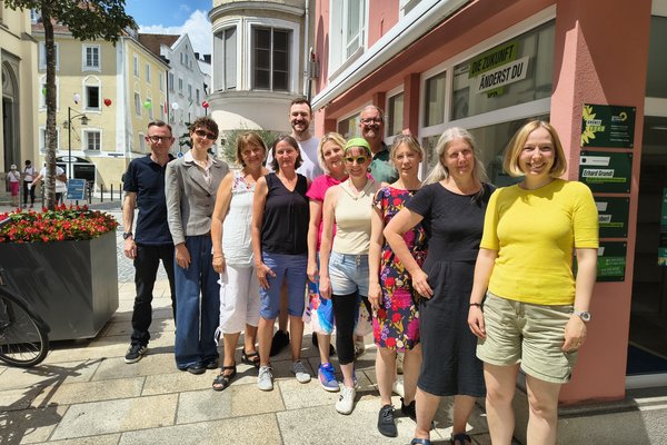 Elf Personen posieren für ein Gruppenfoto. Die Sonne scheint. Die Gruppe steht in einer Gasse der Stadt Passau.