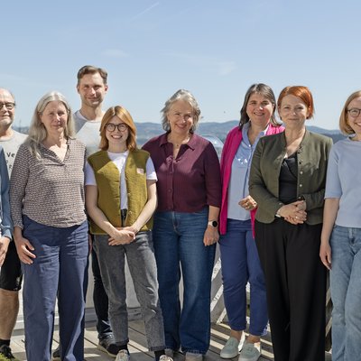 Zehn Personen posieren für ein Gruppenfoto. Sie stehen auf einer Terrasse in der Sonne.
