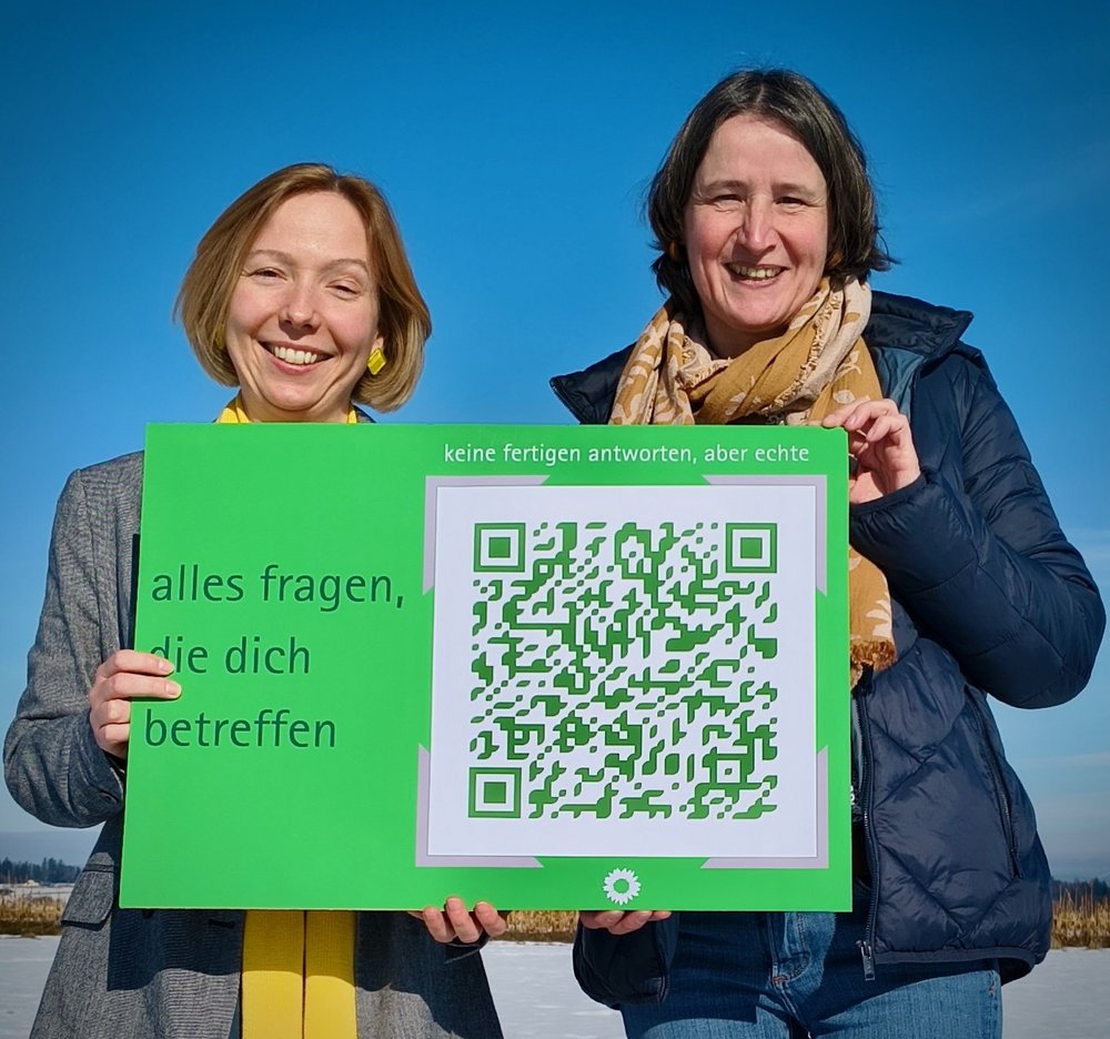 Zwei Frauen halten eine Postkarte im XXL-Format in den Händen. Auf der Postkarte steht "alles fragen, die dich betreffen"