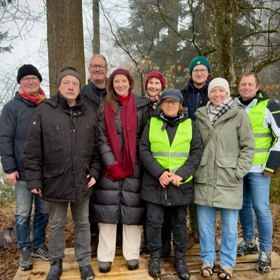 Eine Gruppe von neuen Personen posiert für ein Foto. Sie tragen Winterkleidung und stehen in einem Wald.