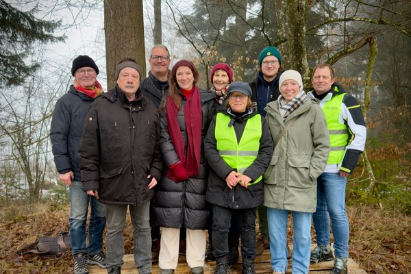 Eine Gruppe von neuen Personen posiert für ein Foto. Sie tragen Winterkleidung und stehen in einem Wald.