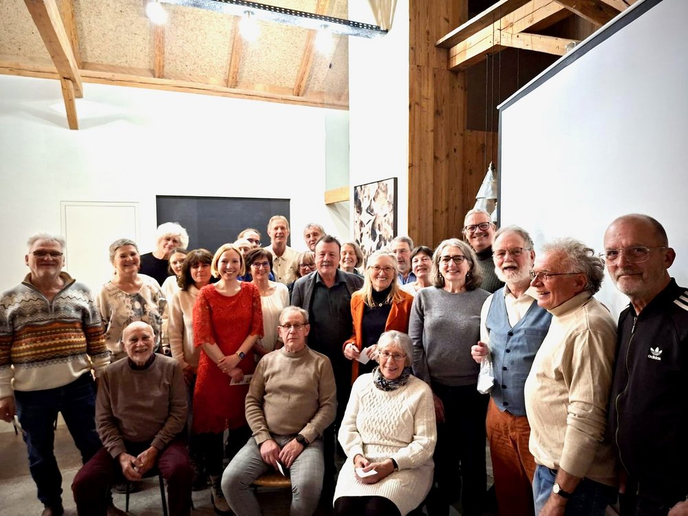 Etwa 30 Personen stehen für ein Gruppenfoto zusammen. Im Vordergrund sitzen drei Personen auf Stühlen.