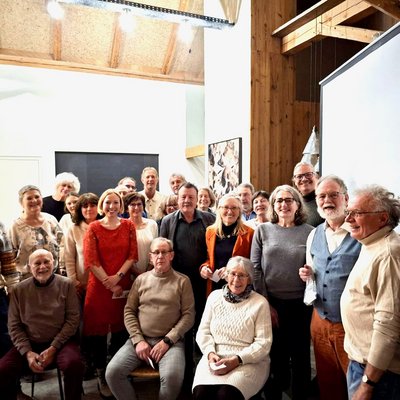 Etwa 30 Personen stehen für ein Gruppenfoto zusammen. Im Vordergrund sitzen drei Personen auf Stühlen.