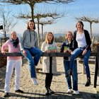 Fünf Frauen posieren für ein Gruppenfoto. Zwei Frauen sitzen auf einem Holzbalken, drei Frauen stehen.