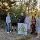 Sechs Personen stehen in einer Lichtung im Wald. Vor ihnen steht eine Tafel mit der Aufschrift "Waldschutz Passauer Land".