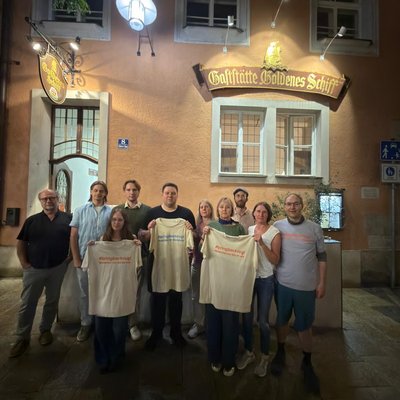 Zehn Personen halten vor dem Gasthaus "Goldenes Schiff" in Passau mehrere T-Shirts mit der Aufschrift "#bringbackrugi"