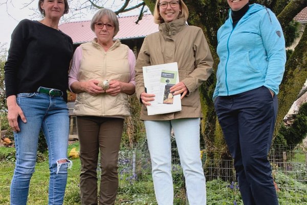 Vier Frauen lächeln in die Kamera. Sie stehen in einem Garten. Sie tragen Pullover und Jacken, es ist Frühling.