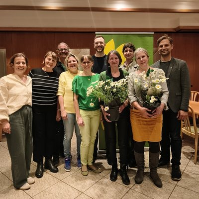 Zehn Personen posieren für ein Gruppenfoto. Zwei Personen halten Blumen in der Hand.
